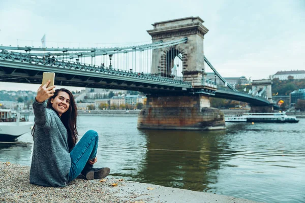 Mooie jonge vrouw zit op strand kant en kijken naar de brug — Stockfoto