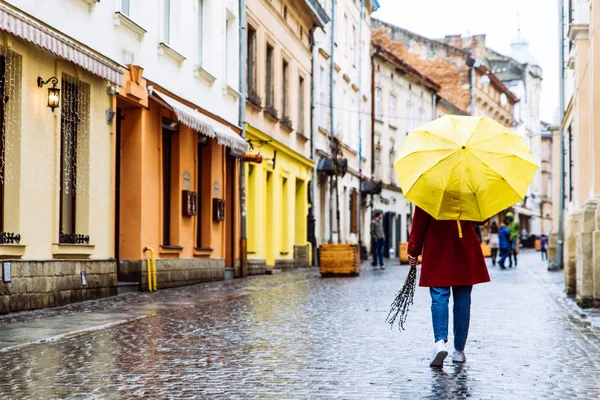 Donna in cappotto rosso con ombrello giallo passeggiata per strada in caso di pioggia. copia spazio — Foto Stock