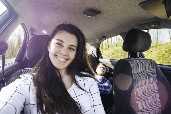 woman making selfie while driving car with slipping man on backseats. car travel concept