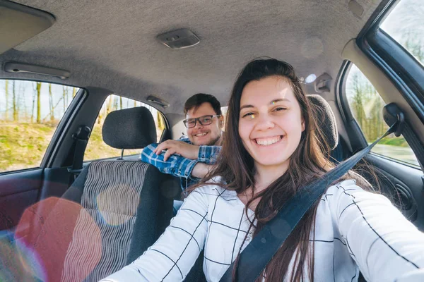 Frau macht Selfie während Autofahrt mit rutschendem Mann auf Rücksitzen. Auto-Reisekonzept — Stockfoto