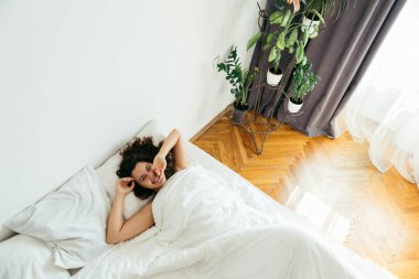 Genç ve güzel bir kadın beyaz çarşaflı parlak bir ışıkla yatakta.