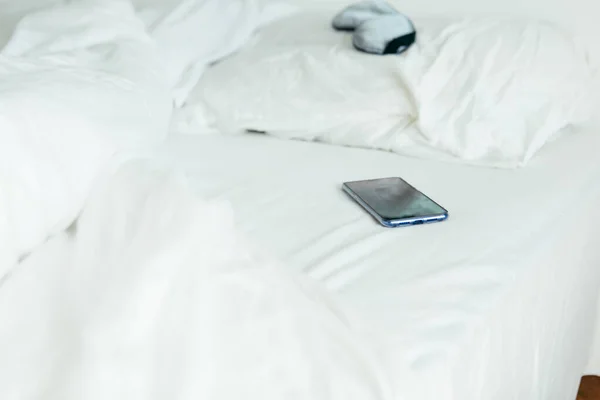 Sovmask med telefon i sängen med vita lakan solig morgon — Stockfoto