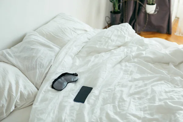 Sleeping mask with phone at bed with white sheets sunny morning — Stock Photo, Image