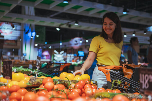 woman choosing yellow tomatoes from store shelf grocery shopping