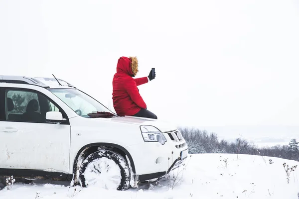 Άνθρωπος κάθεται στο καπό του αυτοκινήτου και γυρίσματα εικόνα της όμορφης θέα το χειμώνα στο τηλέφωνό του — Φωτογραφία Αρχείου