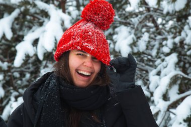 Arka planda bubo köknar ağacı ve kırmızı şapkalı, kışın gülümseyen genç kadının portresi.