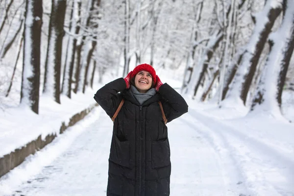 Fiatal csinos mosolygós nő télikabátban piros kalap a városi erdő parkban — Stock Fotó