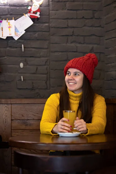 Wanita muda yang bahagia dengan topi merah pakaian musim dingin duduk di kafe minum teh hangat — Stok Foto