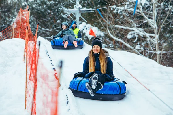 smiling woman on snow tube pulled up by hill