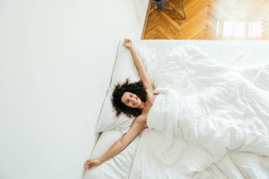 Genç ve güzel bir kadın beyaz çarşaflı parlak bir ışıkla yatakta.