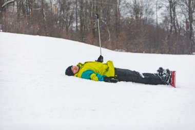 Genç ve gülümseyen bir adam snowboard yaparken kamerada selfie çekiyor.