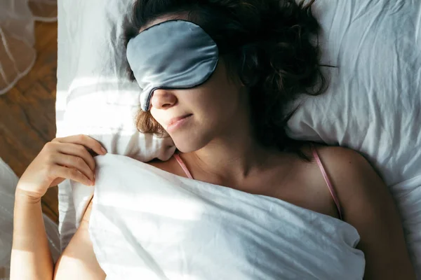 Kvinna sover i mask i sängen starkt ljus i ansiktet — Stockfoto