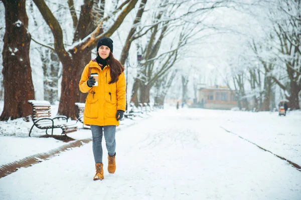 Женщина прогуливается по снежному городскому парку с мыслящим лицом с кофейной чашкой. теплый холодный день — стоковое фото