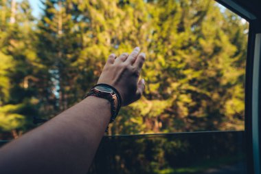 Kadın elini arabanın camından çıkarıp rüzgarın tadını çıkarıyor.