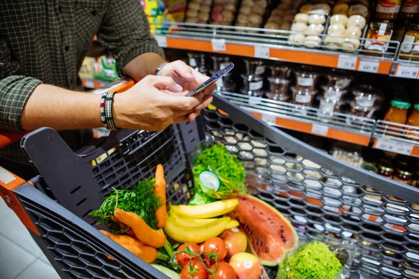 Mann mit Smartphone geht im Supermarkt einkaufen — Stockfoto