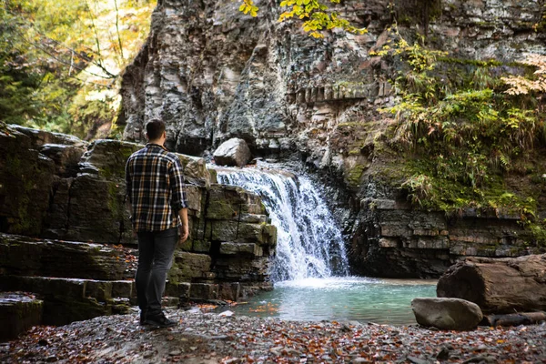 Mężczyzna w kratkę koszula patrząc na jesienny wodospad — Zdjęcie stockowe