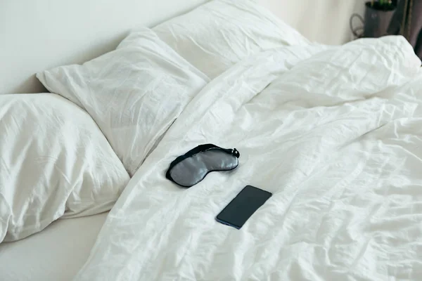 Sleeping mask with phone at bed with white sheets sunny morning — Stock Photo, Image