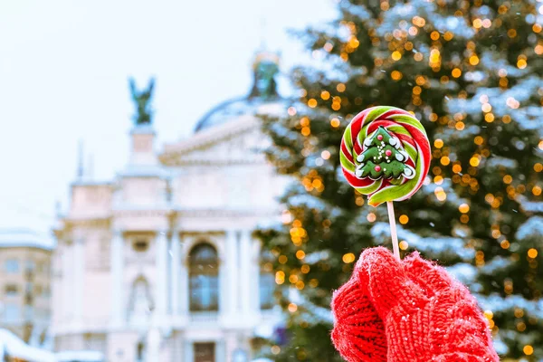 Mano de mujer en guantes rojos sosteniendo caramelos frente al árbol de navidad — Foto de Stock
