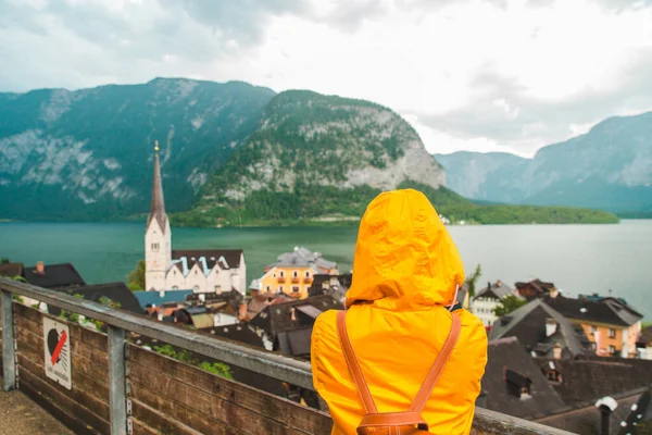 Sarı yağmurluklu kadın Hallstatt şehrine bakıyor. — Stok fotoğraf