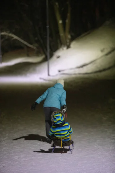 Mãe puxando trenó com criança pelo parque da cidade de inverno — Fotografia de Stock