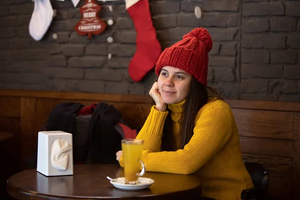 Tânără femeie fericită în costum de iarnă cu pălărie roșie care stă în cafenea și bea ceai cald — Fotografie, imagine de stoc