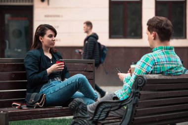 smiling couple sitting on bench talking to each other drinking coffee clipart