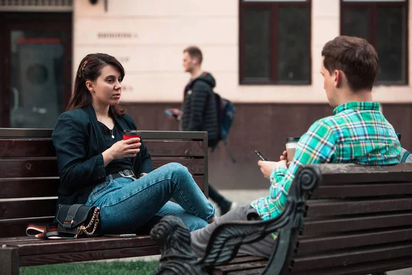 Sonriente pareja sentado en el banco hablando entre sí beber café — Foto de Stock