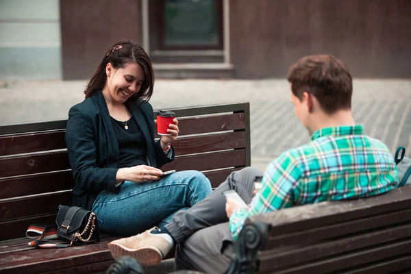 Gülümseyen çift bankta oturup birbirleriyle kahve içerek konuşurken — Stok fotoğraf