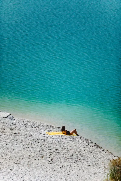 Nő ül homokos strand nézi kék Azúr víz — Stock Fotó