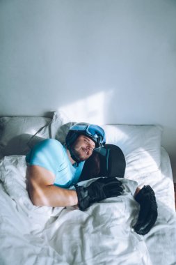 Snowboard kayak yapan bir adam Google ve miğferiyle yatakta.