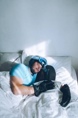 Snowboard kayak yapan bir adam Google ve miğferiyle yatakta.