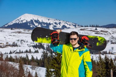 Güneş gözlüklü adam elinde snowboard tutuyor.