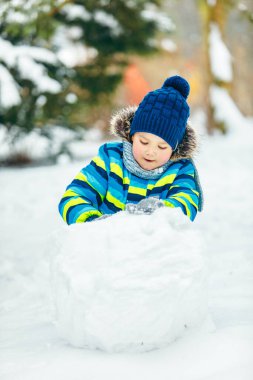 Küçük tatlı çocuk kardan adam yapıyor. yuvarlanan büyük kartopu