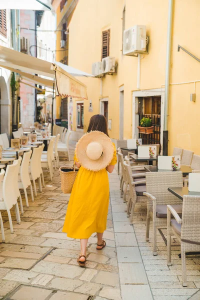 カフェレストランのテーブルの間のリゾートシティストリートを歩く黄色いドレスを着た女性 — ストック写真