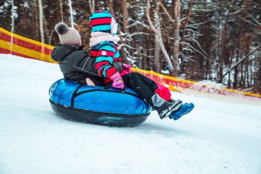 Çocuk sahibi ebeveyn karlı tepenin yanından kar tüpüyle kayıyor.