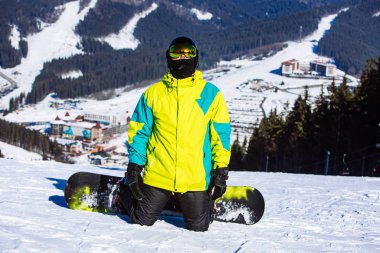 Tepenin tepesinde güneşli bir günde snowboard yapan bir adam.