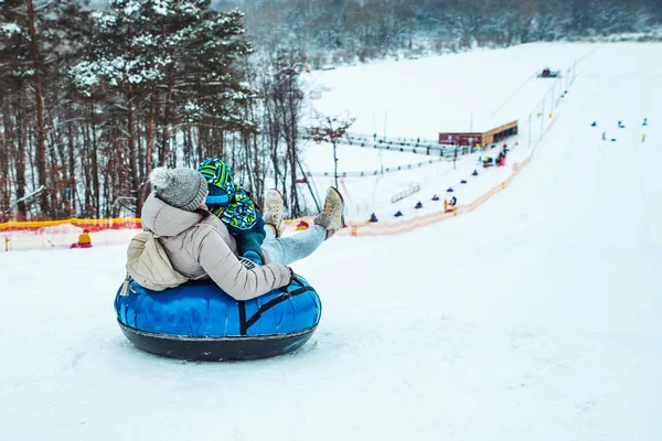 Pai com criança deslizando para baixo por colina nevada com tubo de neve — Fotografia de Stock