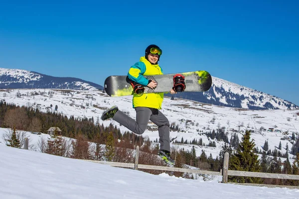 Homem saltando com snowboard em mãos montanhas no fundo — Fotografia de Stock