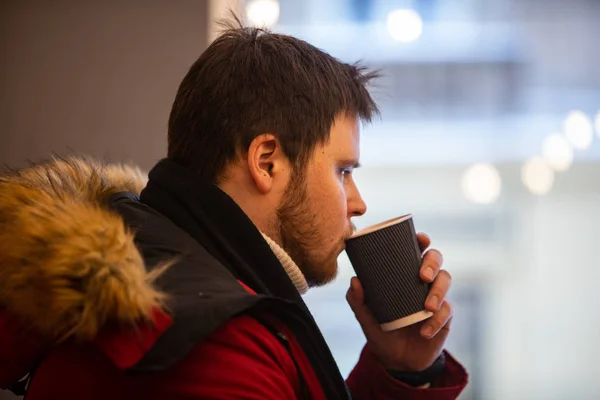 Человек в кафе в красном зимнем пальто пьет чай разогревается — стоковое фото