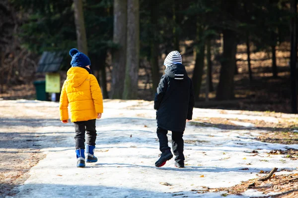 Kışlık elbiseli iki çocuk karlı parkın yanından geçiyor. — Stok fotoğraf