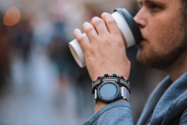 Tek kullanımlık fincandan kahve içen adam. Bileğinde bileklik olan akıllı saat.