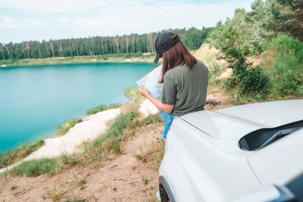 Mulher verificando com mapa no lago capuz do carro SUV com água azul no fundo — Fotografia de Stock