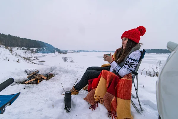 Giovane bella donna adulta seduta sulla sedia vicino al fuoco del campo in inverno — Foto Stock