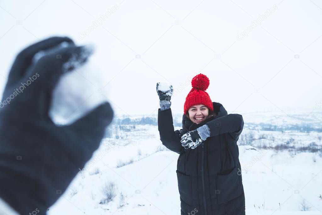 couple playing outdoors in winter time. woman throwing snowball. man first point view