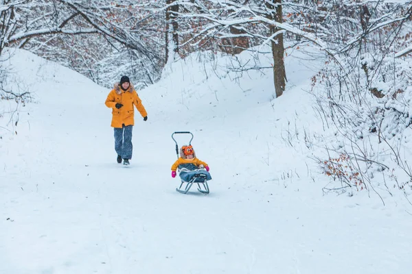 Pai com filha em casacos de inverno amarelos deslizando colina nevada — Fotografia de Stock