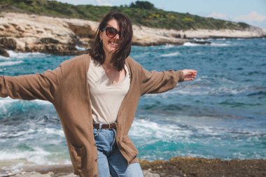 Deniz kıyısında doğanın gücünün tadını çıkaran bir kadın. Rüzgarlı hava