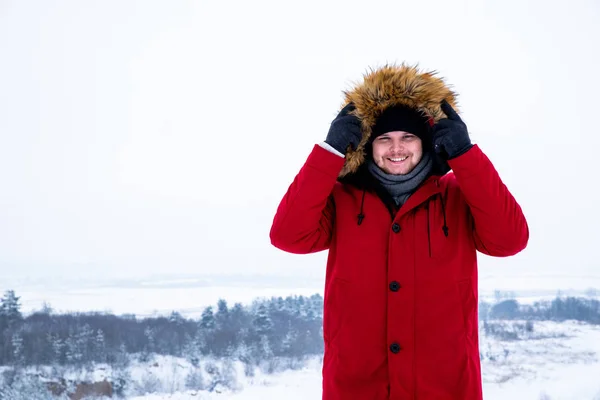 Man in red winter coat with fur hood snowed field on background — Stock Photo, Image