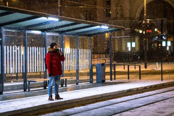 Hombre de abrigo rojo de invierno de pie en la parada de tranvía de autobús a la espera de transporte público — Foto de Stock