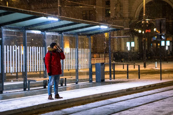 Άνδρας με κόκκινο παλτό χειμώνα στέκεται στη στάση του τραμ λεωφορείο περιμένει για τα μέσα μαζικής μεταφοράς — Φωτογραφία Αρχείου