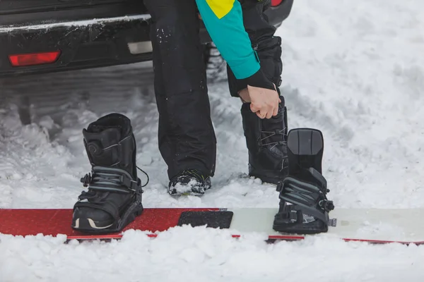 Hombre cambiando botas regulares a snowboard en el lugar de estacionamiento cerca del coche — Foto de Stock